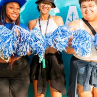 students posing in front of CAB backdrop at Laker Kickoff photo booth with pom poms smiling